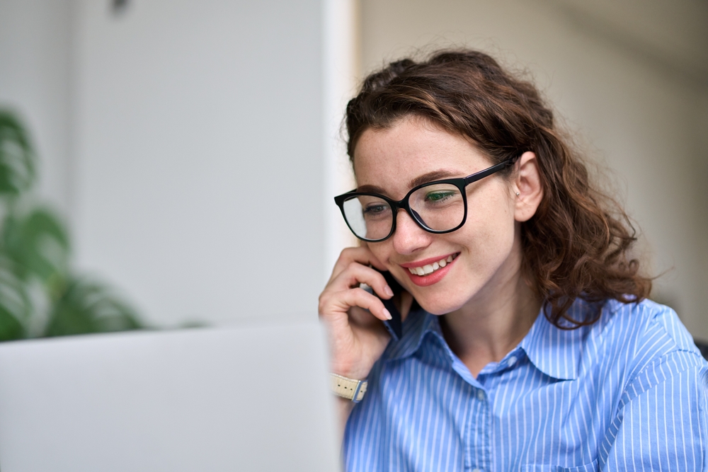 Young,woman,sales,manager,talking,on,cell,phone,using,laptop